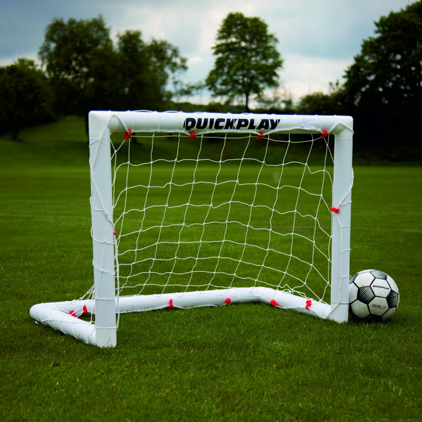 Porticina da calcio pieghevole Q-FOLD 90 x 75 cm con telaio e rete bianchi sull'erba, con un pallone accanto.