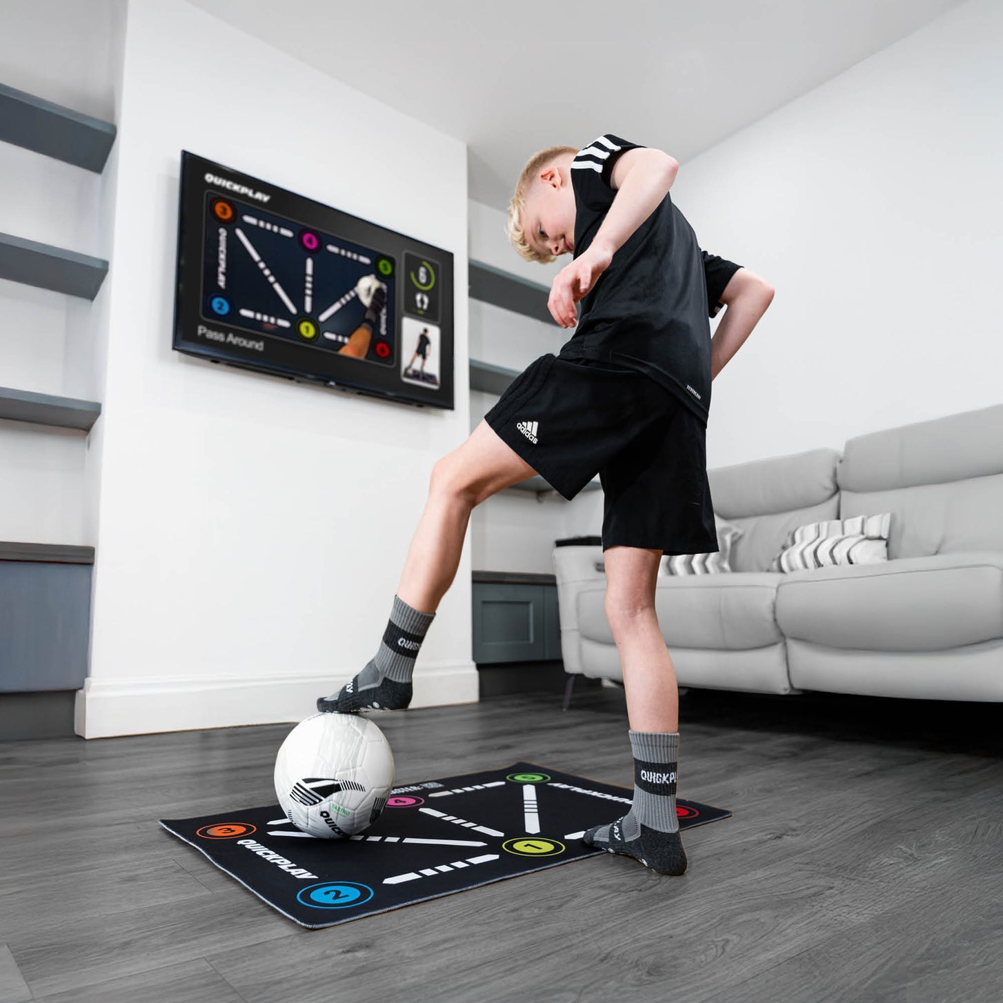 Tappetino da calcio per il controllo palla in soggiorno, bambino con calze grip che lavora la palla mentre la TV mostra un esercizio.
