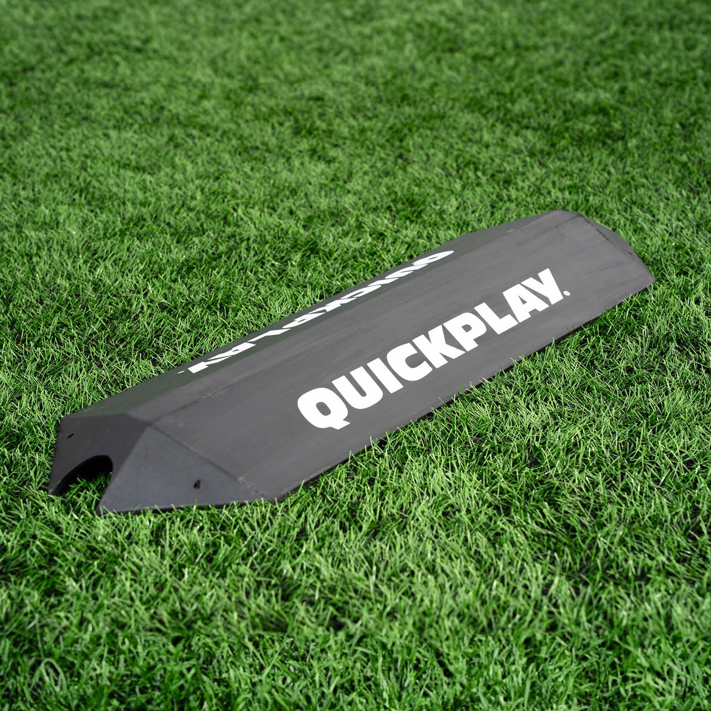 Deviatore a rampa per l'allenamento dei portieri, un cuneo nero con un logo QUICKPLAY bianco, appoggiato su erba sintetica.