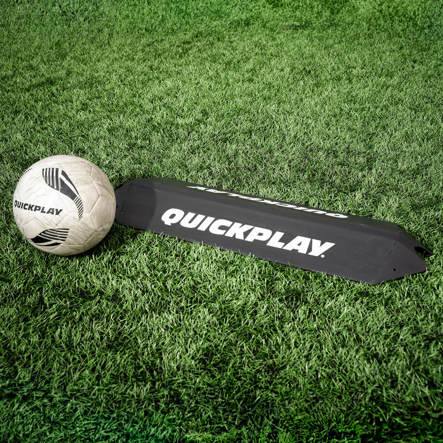 Deviatore a rampa per l'allenamento dei portieri su erba sintetica, con un pallone bianco QUICKPLAY appoggiato a un'estremità.