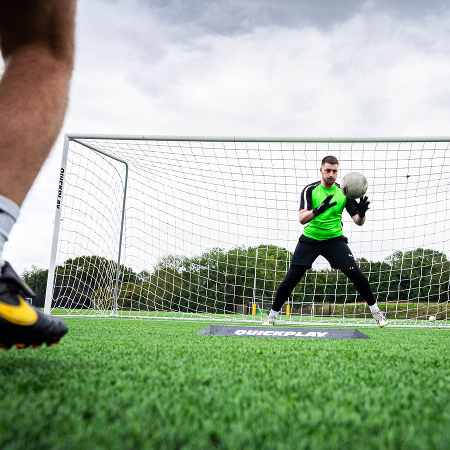 Portiere che blocca una palla all'altezza del petto davanti a una porta, con il deviatore a rampa per l'allenamento dei portieri sull'erba.