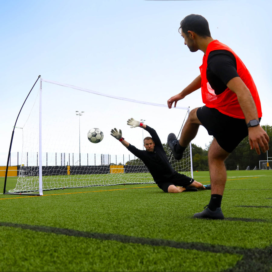 Porta KICKSTER Elite 370 x 180 cm ripresa a livello del campo, con un portiere che si allunga per parare il tiro di un giocatore con la casacca arancione.