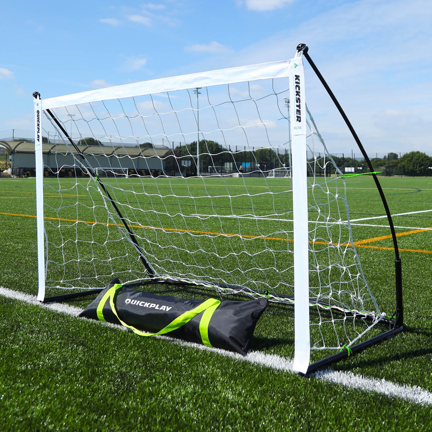 Porta KICKSTER Elite 150 x 100 cm su un campo in erba sintetica, con la sua borsa per il trasporto nera QUICKPLAY davanti.