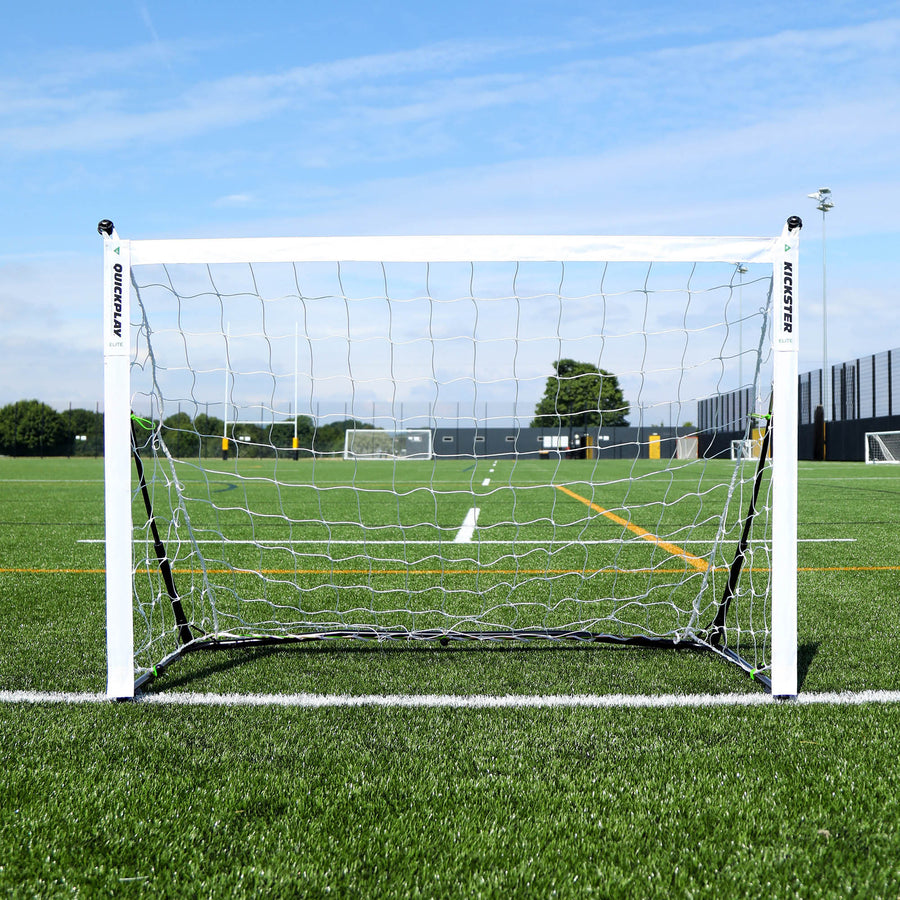 Porta KICKSTER Elite 150 x 100 cm vista frontalmente, con una rete bianca, sulla linea di un campo in erba sintetica.