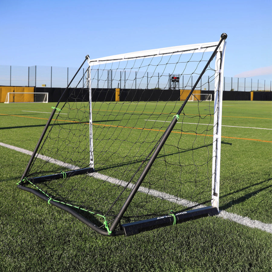 Porta KICKSTER Elite 150 x 100 cm vista da un angolo posteriore su un campo in erba sintetica, con il telaio nero e le fascette verdi.