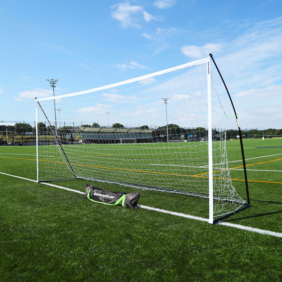 Porta KICKSTER Elite 500 x 200 cm su un campo in erba sintetica, vista in diagonale con la sua borsa per il trasporto nera QUICKPLAY davanti.