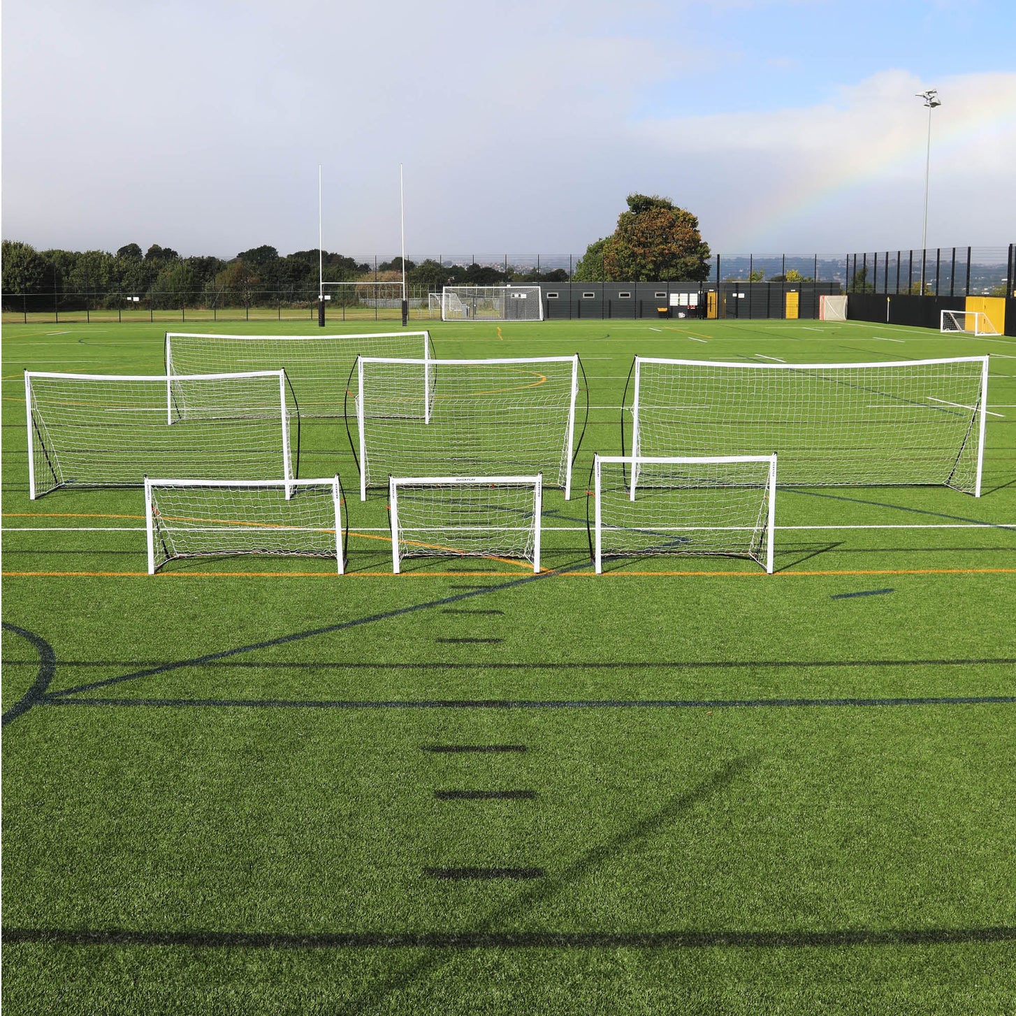 Porta da calcio a 5 KICKSTER Elite 300 x 200 cm insieme a una gamma di porte bianche QUICKPLAY di diverse misure su un campo.