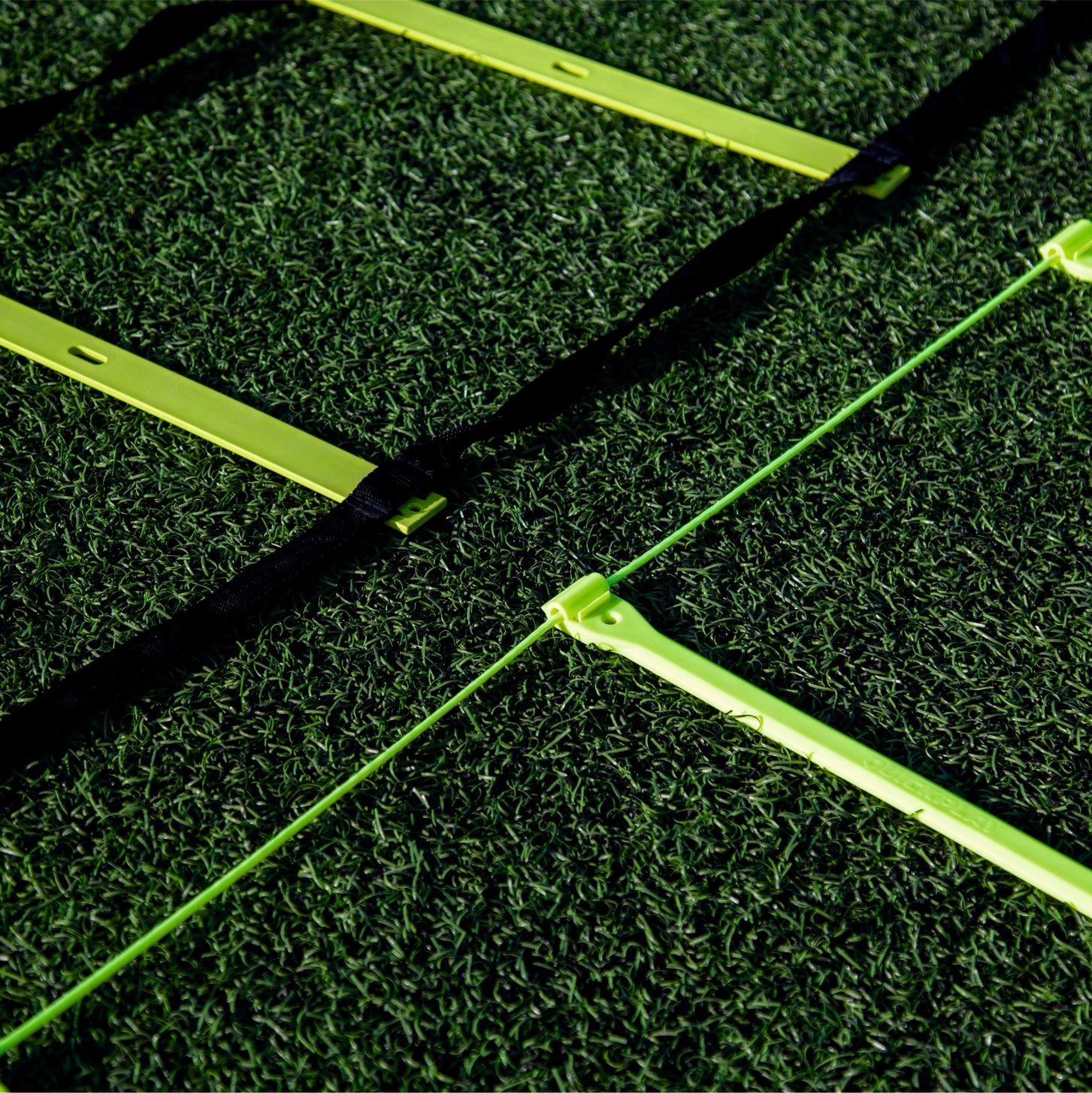 Primo piano dei pioli gialli della scaletta di agilità su erba sintetica, una scaletta con cinghie nere e una con un sottile cordino verde.