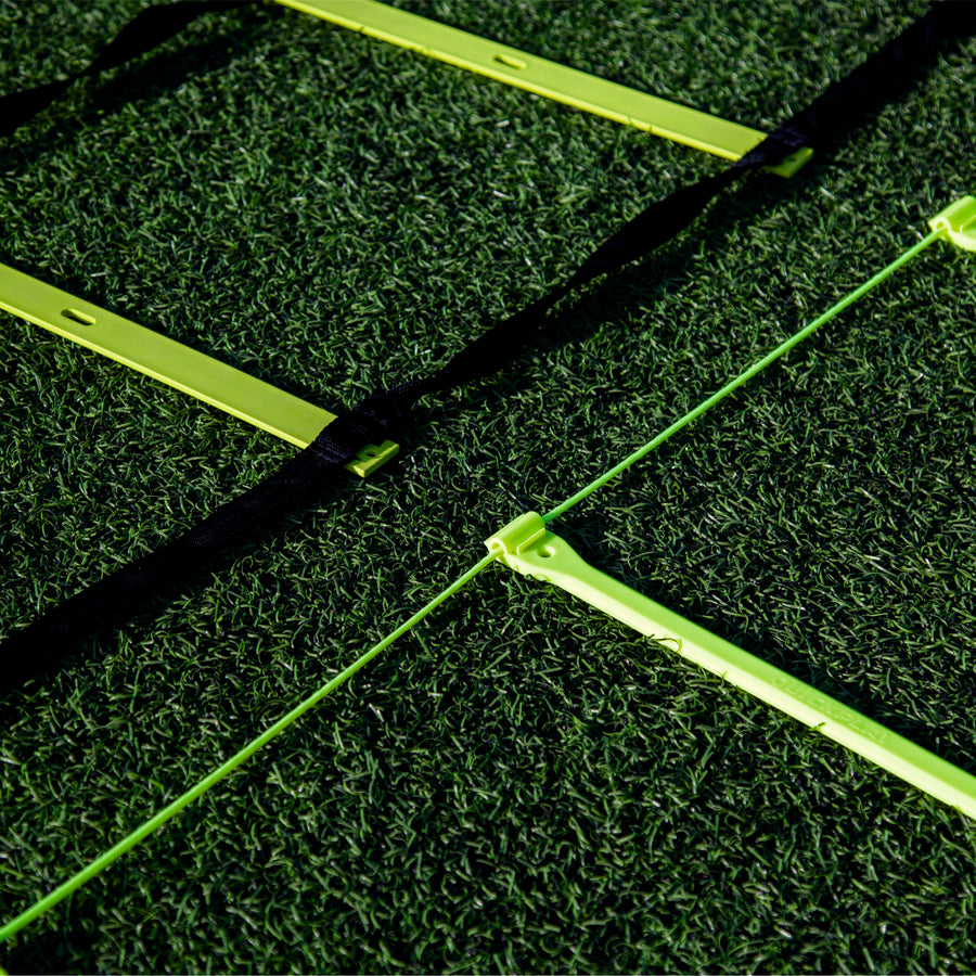 Primo piano dei pioli gialli della scaletta di agilità su erba sintetica, una scaletta con cinghie nere e una con un sottile cordino verde.