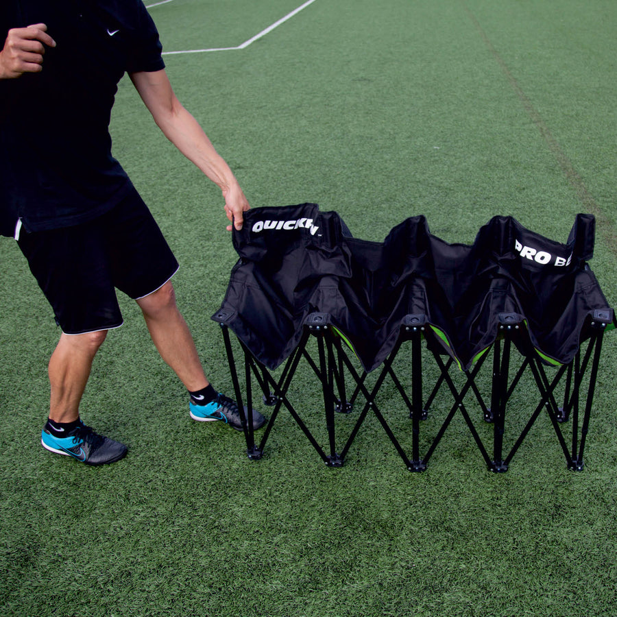 Persona che apre la panchina PRO Bench 4 posti nera su un campo in erba sintetica.