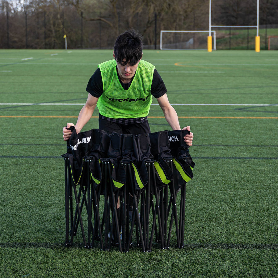 Giocatore con una casacca verde QUICKPLAY che regge la panchina PRO Bench 6 posti parzialmente chiusa su un campo in erba sintetica.