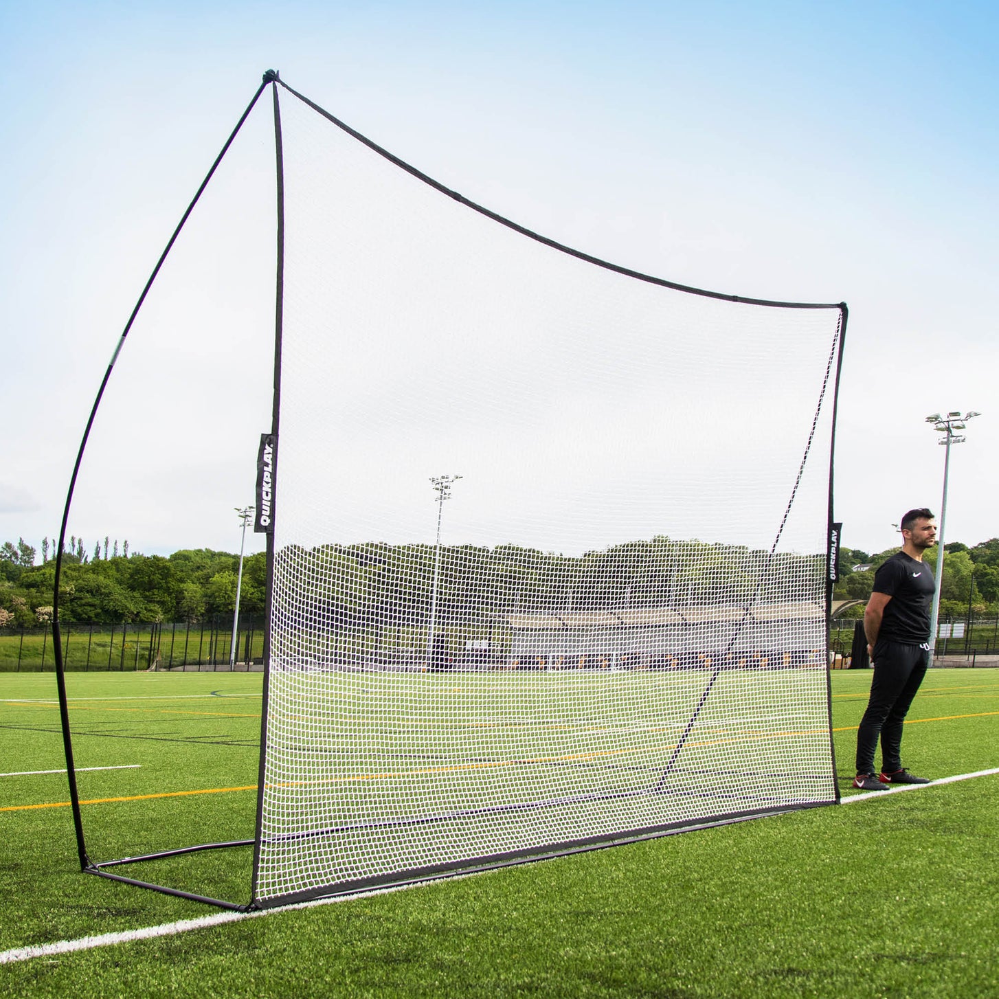 Rete parapalloni MEGA NET 370 x 270 cm con telaio nero e rete bianca su un campo in erba sintetica, con un uomo in piedi accanto.