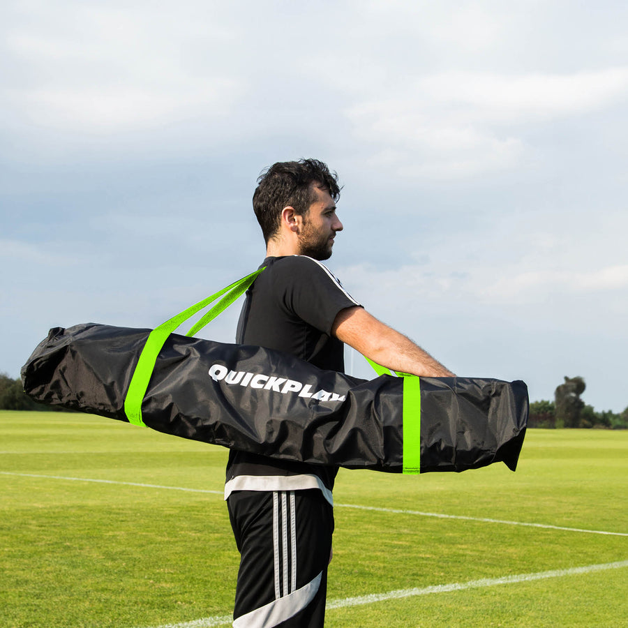 Uomo che porta la MEGA NET 370 x 270 cm nella sua borsa nera QUICKPLAY con cinghie verdi su un campo in erba.