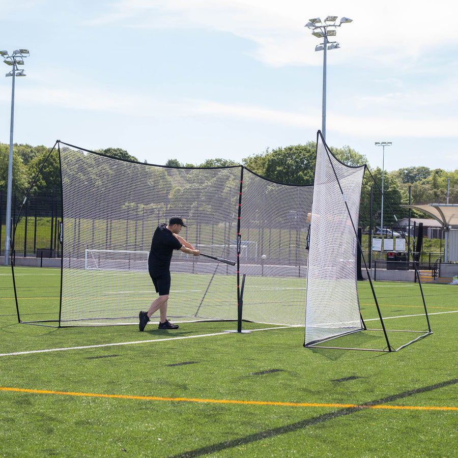 Reti parapalloni MEGA NET 370 x 270 cm su un campo in erba sintetica, con un giocatore che colpisce una palla da baseball con una mazza verso le reti.