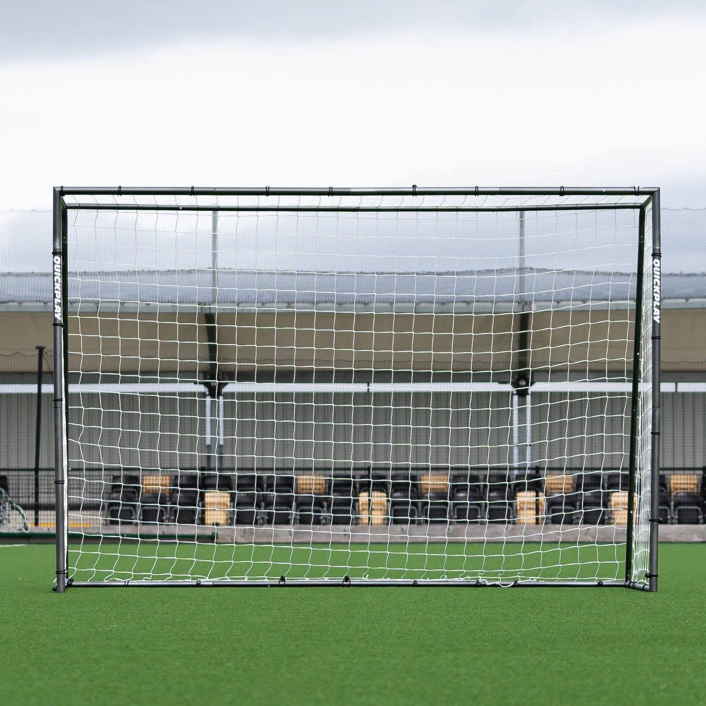 Porta da calcio a 5 GS Series 300 x 200 cm vista frontalmente, davanti a una tribuna di un campo in erba sintetica.
