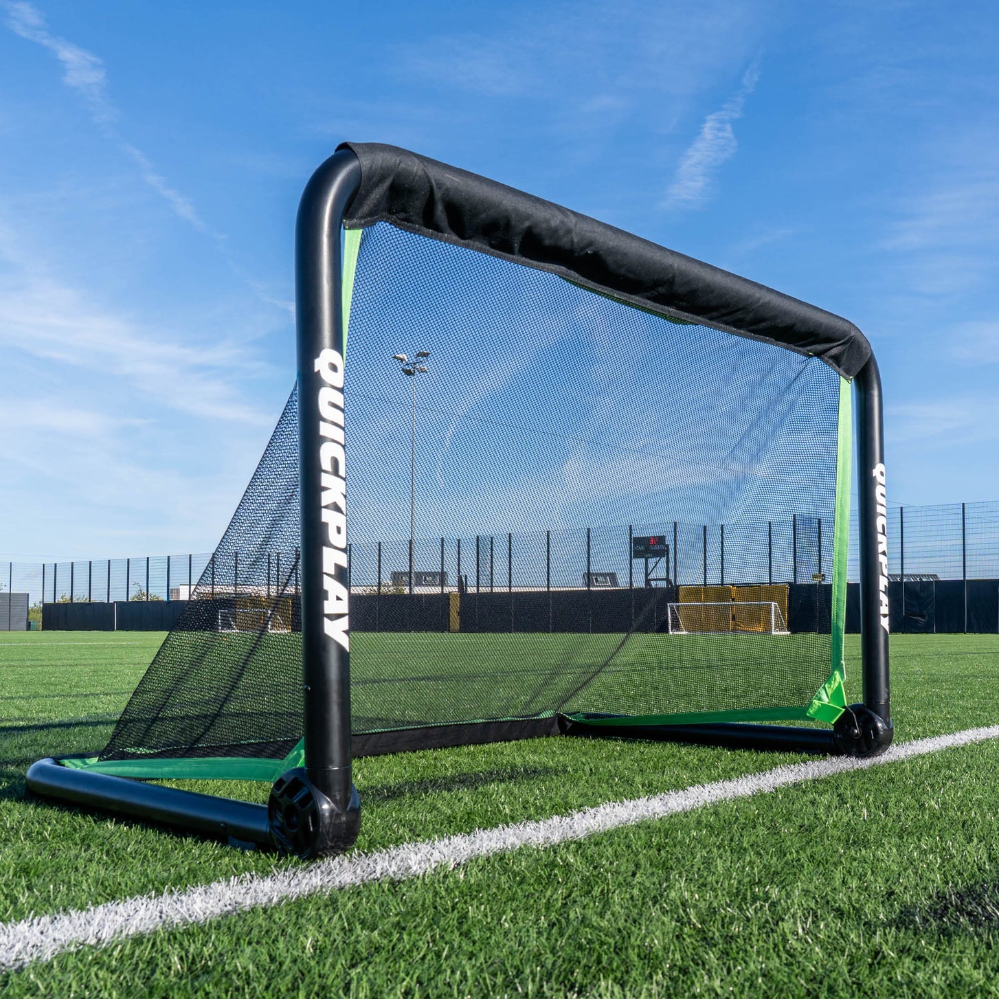 Porta da calcio RHINO 120 x 75 cm con telaio nero spesso e rete nera, sulla linea di un campo in erba sintetica.