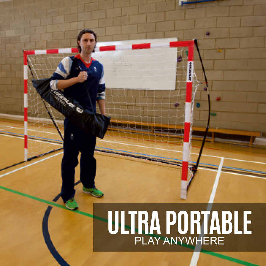 Uomo con una borsa nera QUICKPLAY davanti alla porta da pallamano portatile per bambini 240 x 170 cm in un palazzetto, con la scritta "ultra portable".
