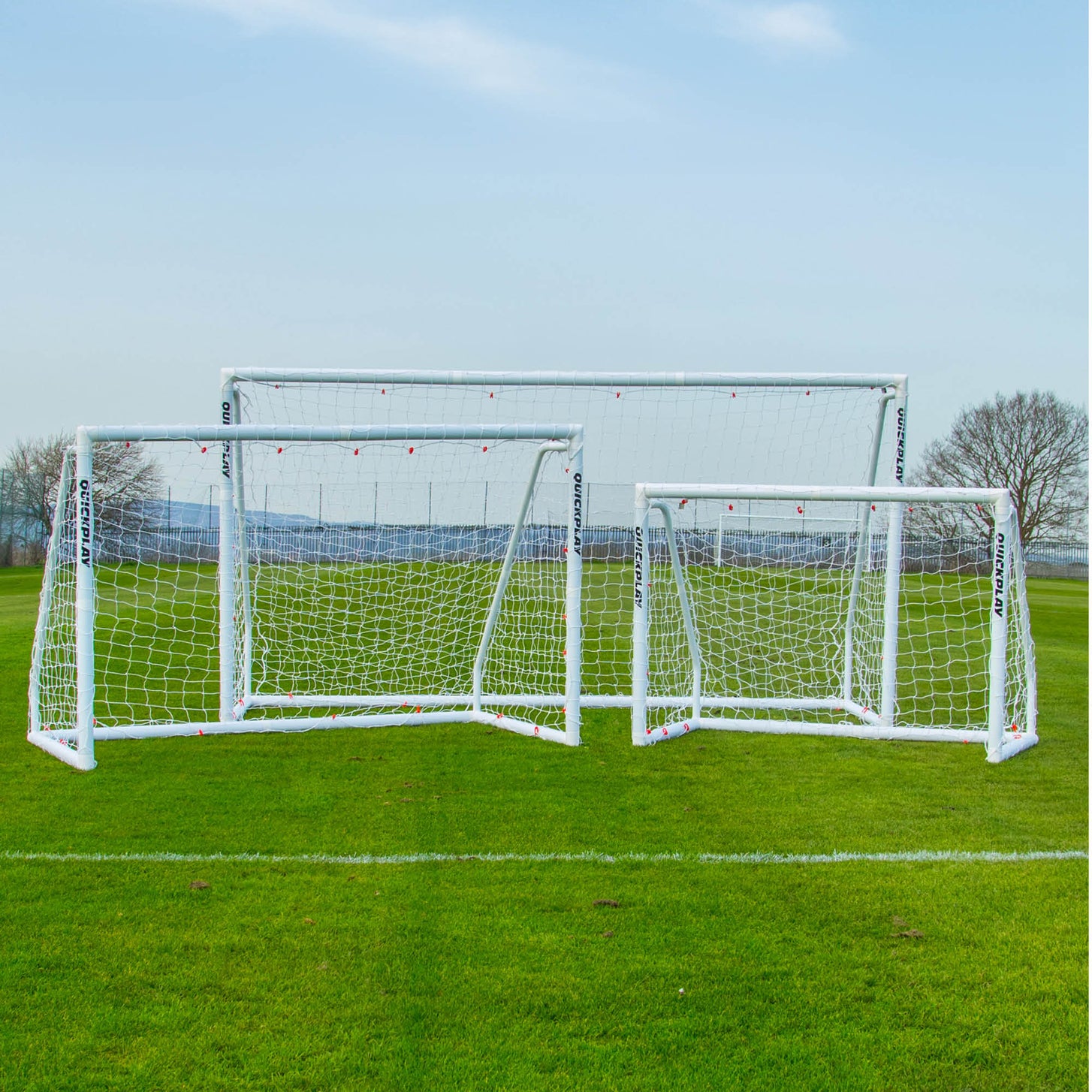 Porta Q-FOLD Match 370 x 180 cm con due porte bianche Q-FOLD Match più piccole, una accanto all'altra su un campo in erba.