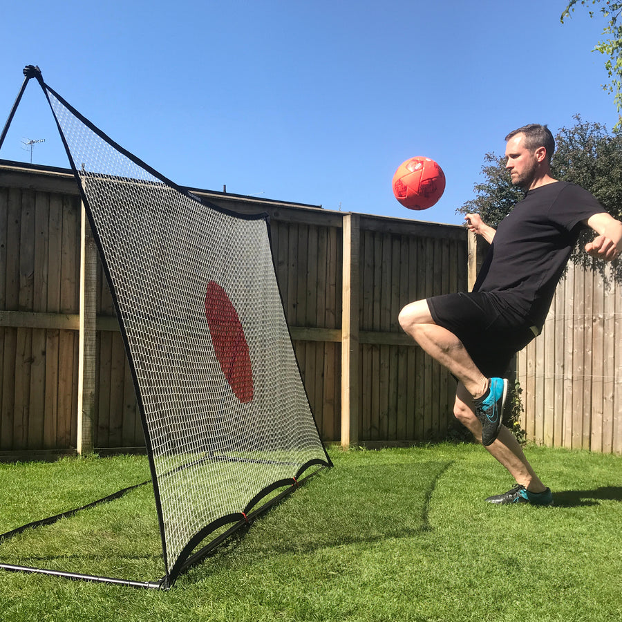 Uomo che controlla una palla rossa rimandata dal rebounder da calcio SPOT 240 x 150 cm in un giardino recintato, rete con bersaglio rosso.