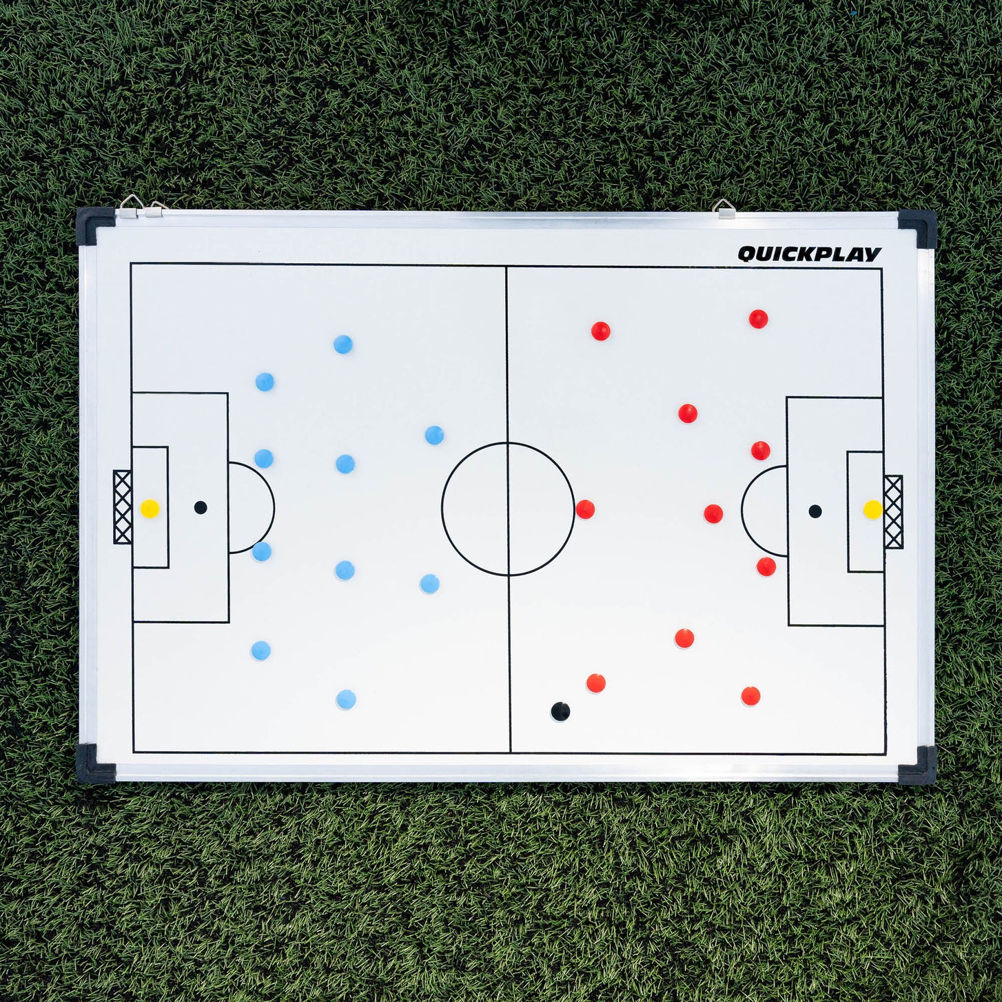Lavagna tattica magnetica da calcio 60 x 90 cm distesa su erba sintetica, con le squadre di magneti rossi e blu schierate.