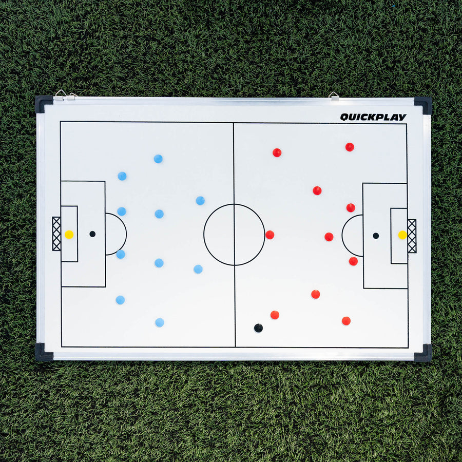 Lavagna tattica magnetica da calcio 60 x 90 cm distesa su erba sintetica, con le squadre di magneti rossi e blu schierate.