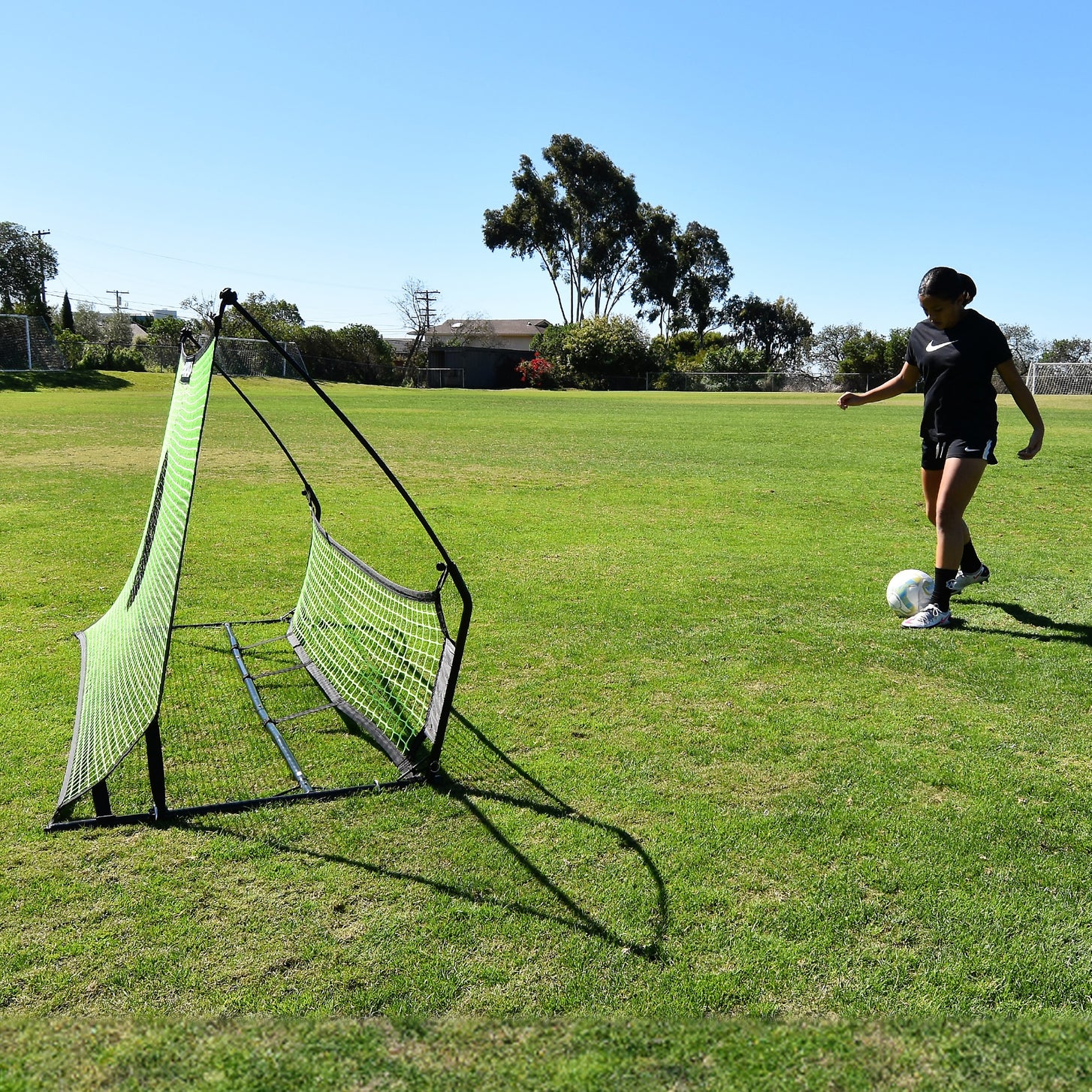 Giocatore che sta per passare una palla nel rebounder da calcio a doppia rete TEKKERS Trainer, visto di lato sull'erba.