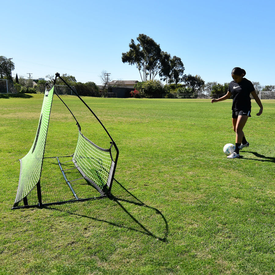 Giocatore che sta per passare una palla nel rebounder da calcio a doppia rete TEKKERS Trainer, visto di lato sull'erba.