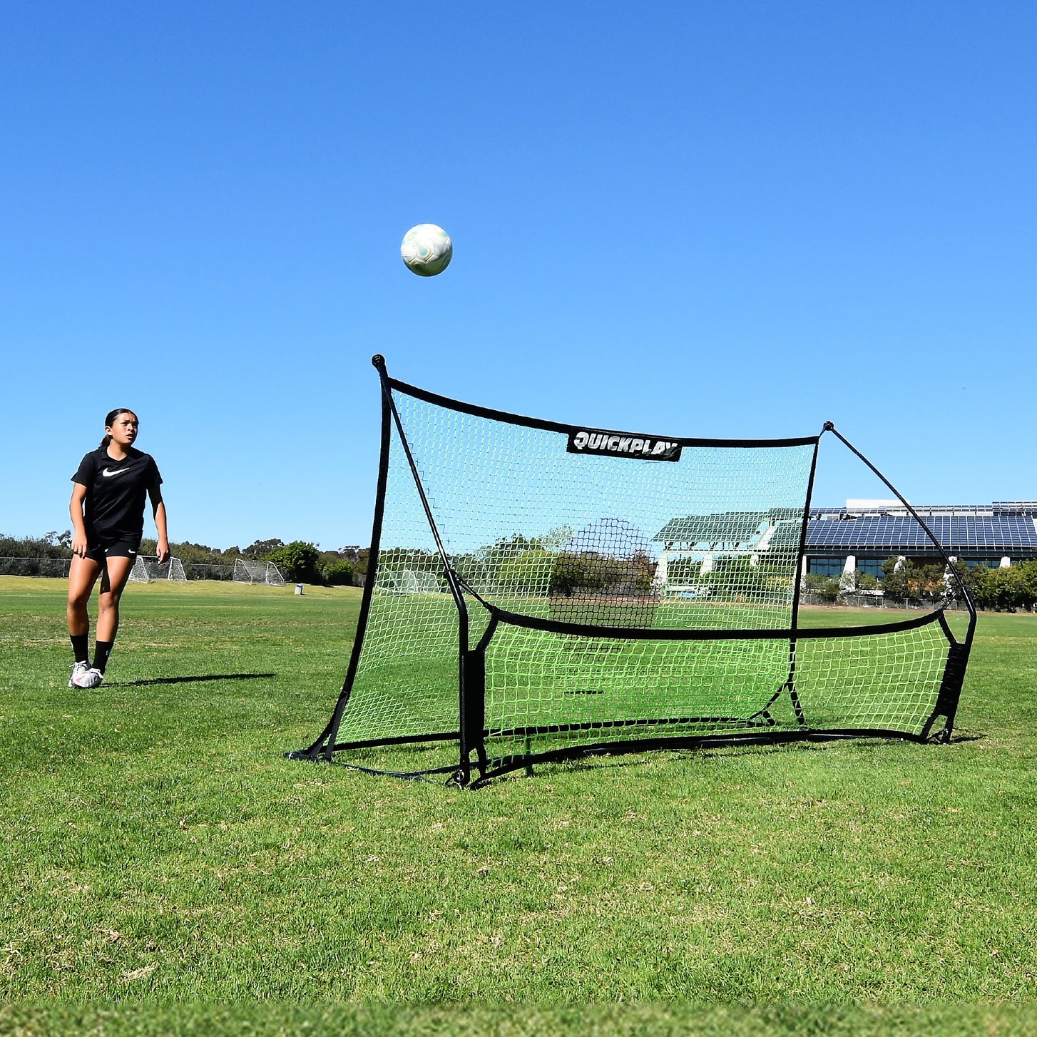 Giocatore che osserva una palla che si alza dalla rete del TEKKERS Trainer, vista frontale del rebounder su un campo in erba.