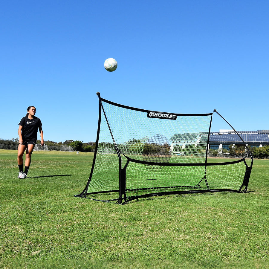 Giocatore che osserva una palla che si alza dalla rete del TEKKERS Trainer, vista frontale del rebounder su un campo in erba.